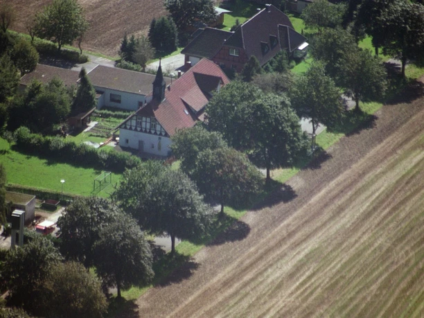 broederhausen-schule-broederhausen-heute.JPG Luftaufnahme eines Bauernhauses mit Satteldach und Fachwerk, umgeben von Bäumen und Feldern.