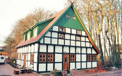 broederhausen-fam-steinmann.jpg Fachwerkhaus mit rotem Satteldach und grüner Giebelwand, umgeben von Bäumen und gepflastertem Hof.