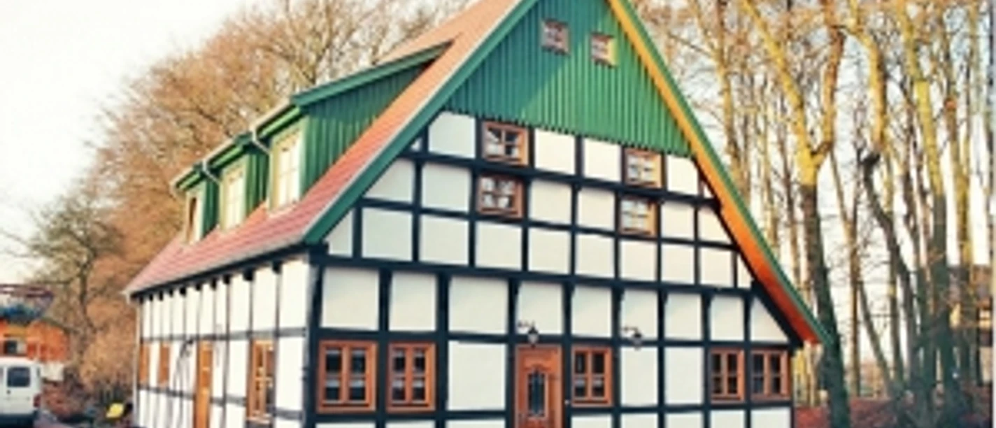 broederhausen-fam-steinmann.jpg Fachwerkhaus mit rotem Satteldach und grüner Giebelwand, umgeben von Bäumen und gepflastertem Hof.