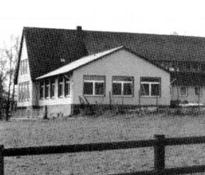 buettendorf-dorfgemeinschaftsraum.jpg Ein schlichtes Gebäude mit Satteldach, großen Fenstern und anliegendem Rasen streckt sich in ländlicher Umgebung.