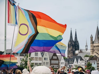 Cologne Pride Regenbogenfahnen wehen im Vordergrund, während der Kölner Dom markant im Hintergrund zu sehen ist. Menschen sind dabei, den Cologne Pride zu feiern.Rainbow flags fly in the foreground, while Cologne Cathedral can be seen prominently in the background. People are celebrating Cologne Pride.