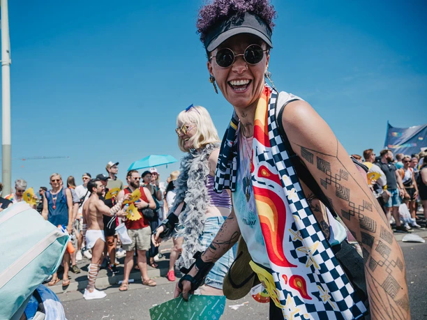 Cologne Pride Menschen genießen in bunter Kleidung und gelöster Atmosphäre den Cologne Pride unter blauem Himmel.