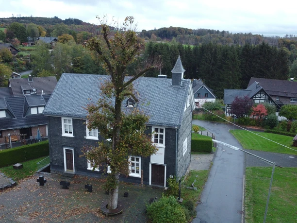 KKH aus der Luft Historisches zweistöckiges Steinhaus mit markantem Schieferdach, von Bäumen und Wiesen umgeben.