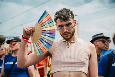 Cologne Pride A young man in a sleeveless top poses confidently with a colorful fan.