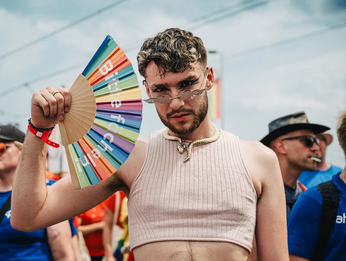 Cologne Pride Ein junger Mann in einem ärmellosen Oberteil posiert selbstbewusst mit einem bunten Fächer.A young man in a sleeveless top poses confidently with a colorful fan.