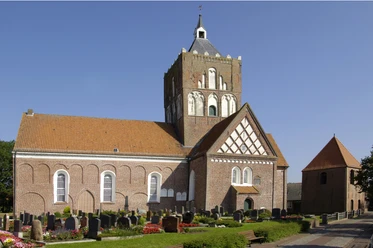 Kirche Pilsum Imposante Kreuzkirche Pilsum mit massivem Vierungsturm und Friedhof unter blauem Himmel.