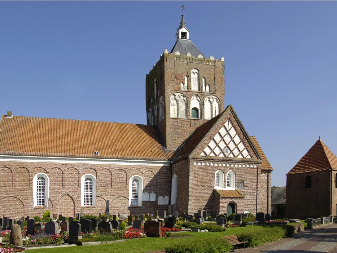 Kirche Pilsum Imposante Kreuzkirche Pilsum mit massivem Vierungsturm und Friedhof unter blauem Himmel.