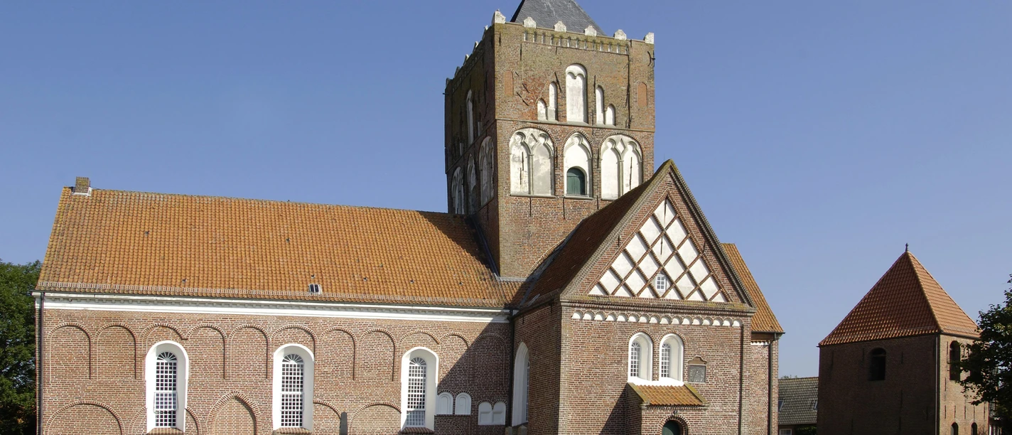 Kirche Pilsum Imposante Kreuzkirche Pilsum mit massivem Vierungsturm und Friedhof unter blauem Himmel.
