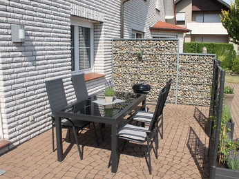Modern möblierte Terrasse auf Pflastersteinen, geschützt durch Sichtschutz und umgeben von Ziegelhaus.