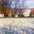 holsen.jpg Fachwerkhäuser in einer ländlichen Landschaft mit Bäumen und teils schneebedeckten Wiesen im Vordergrund.