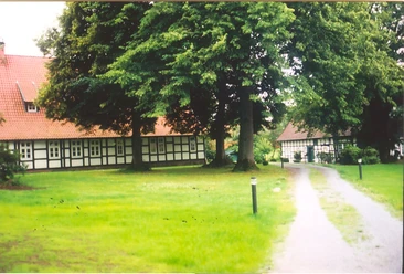 holsen-hof-sielermann-heute.jpg Ein historischer Hof mit Fachwerkgebäuden, umgeben von grünem Rasen und großen alten Bäumen.