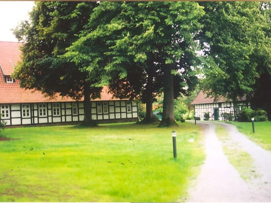 holsen-hof-sielermann-heute.jpg Ein historischer Hof mit Fachwerkgebäuden, umgeben von grünem Rasen und großen alten Bäumen.
