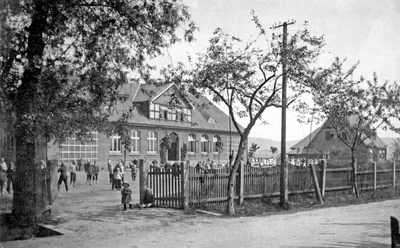huellhorst-alte-schule-01.jpg Historisches Schulgebäude mit Ziegelsteinfassade, umgeben von Bäumen und Menschen im Vordergrund.