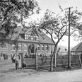 huellhorst-alte-schule-01.jpg Historisches Schulgebäude mit Ziegelsteinfassade, umgeben von Bäumen und Menschen im Vordergrund.