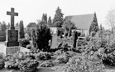 huellhorst-neuer-freidhof.jpg Ein stilvoller Friedhof mit gepflegten Gräbern und üppiger Bepflanzung, flankiert von Bäumen.