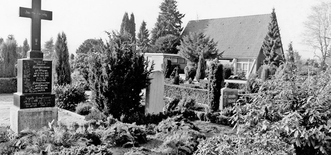 huellhorst-neuer-freidhof.jpg Ein stilvoller Friedhof mit gepflegten Gräbern und üppiger Bepflanzung, flankiert von Bäumen.