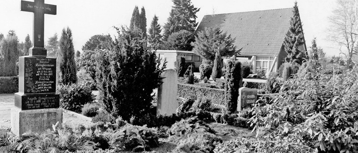 huellhorst-neuer-freidhof.jpg Ein stilvoller Friedhof mit gepflegten Gräbern und üppiger Bepflanzung, flankiert von Bäumen.