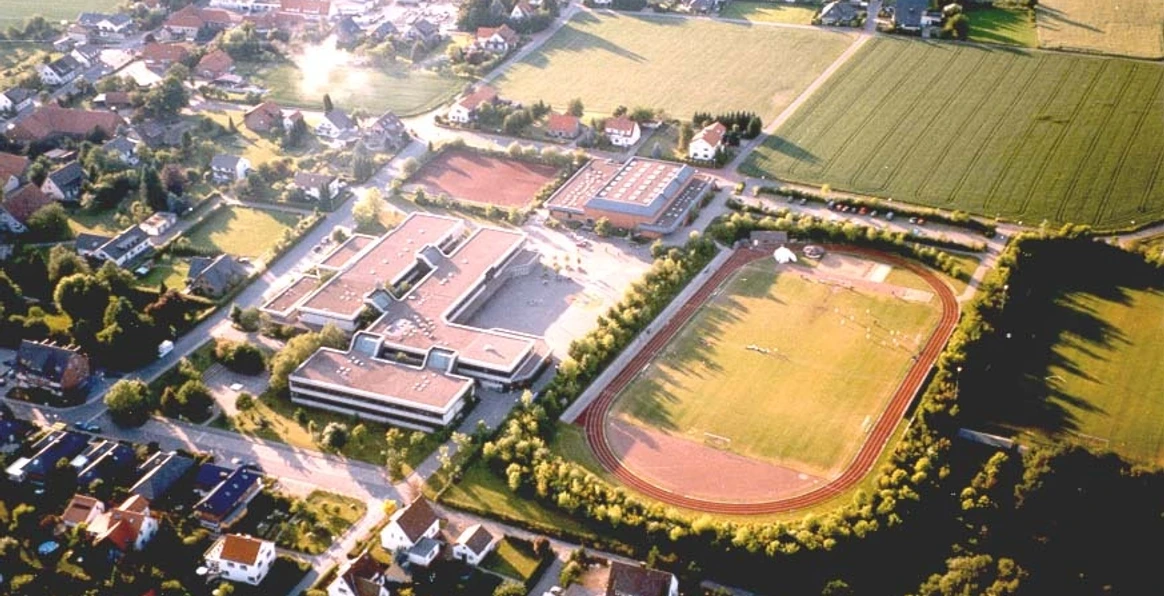 huellhorst-gesamtschule.jpg Luftaufnahme einer Schule in einer ländlichen Gegend mit Sportplatz, umgeben von Feldern und Wohnhäusern.