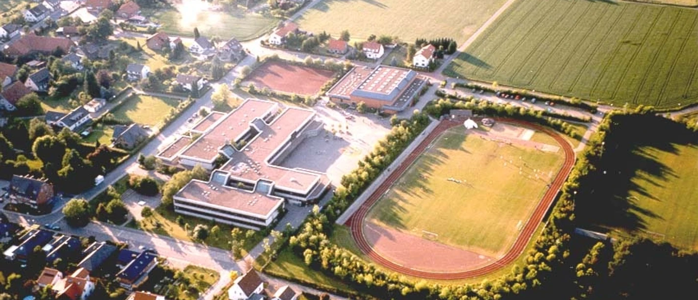huellhorst-gesamtschule.jpg Luftaufnahme einer Schule in einer ländlichen Gegend mit Sportplatz, umgeben von Feldern und Wohnhäusern.