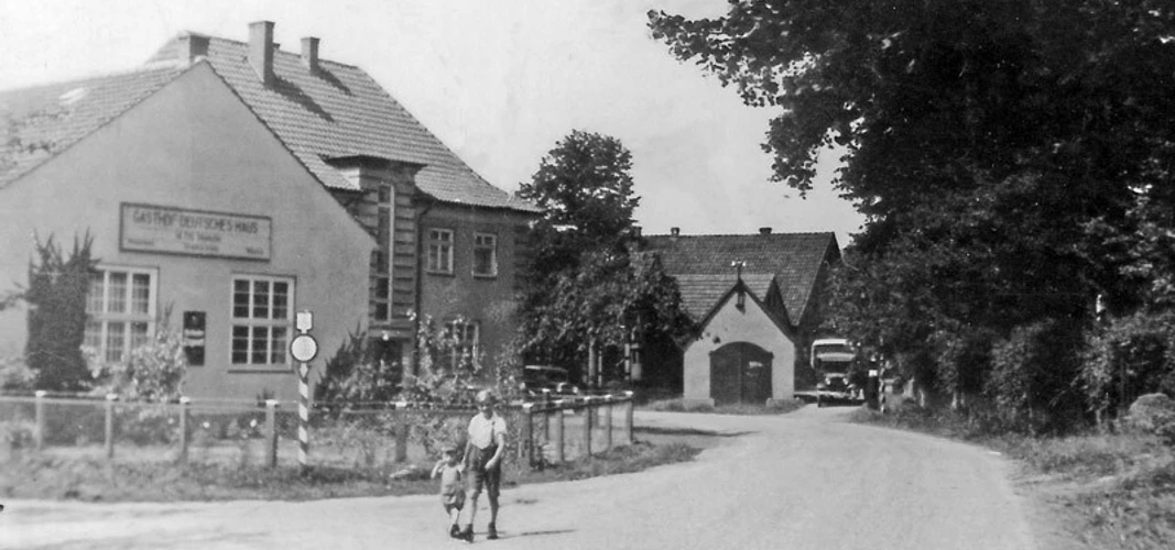 huellhorst-altes-spritzenhaus.jpg Historisches Gebäude mit Fachwerk und Satteldach, umgeben von Bäumen und Blumen, bei klarem Himmel.
