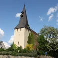 Andreaskirche Hüllhorst Die Andreaskirche Hüllhorst mit spitzem Kirchturm, umgeben von grünen Bäumen und blauem Himmel.