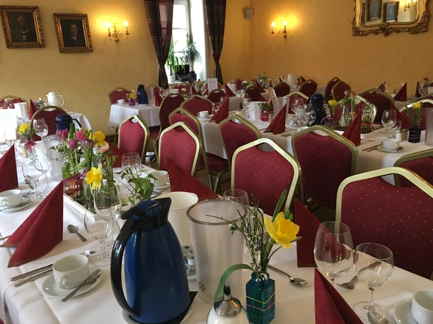 Titelbild Elegantly gedeckter Saal mit rot gepunkteten Stühlen, weißen Tischdecken und bunter Blumendekoration.