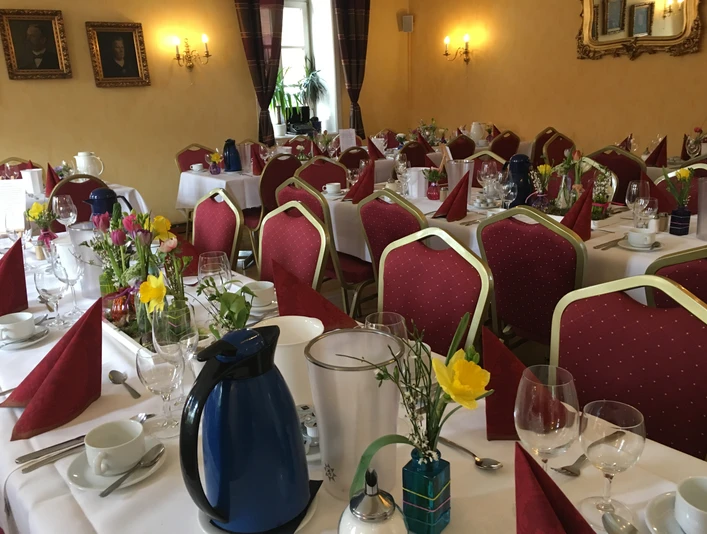 Titelbild Elegantly gedeckter Saal mit rot gepunkteten Stühlen, weißen Tischdecken und bunter Blumendekoration.