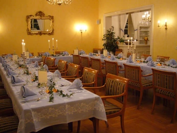 Festsaal Geschmückter Festsaal mit langen, gedeckten Tischen, Kerzenleuchtern und eleganten Holzstühlen.