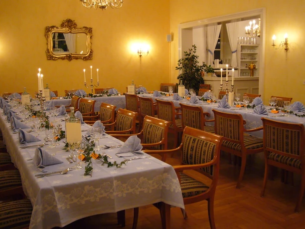 Festsaal Geschmückter Festsaal mit langen, gedeckten Tischen, Kerzenleuchtern und eleganten Holzstühlen.