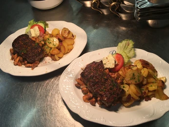 Slideshow2 Zwei Teller mit saftigem Steak auf Pilzen, dazu knusprige Bratkartoffeln und frisches Gemüse.