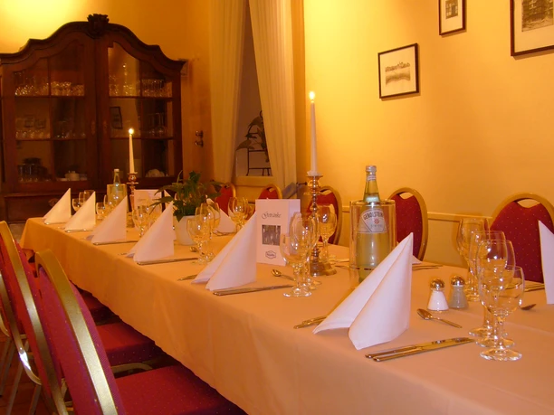Slideshow3 Eine lange, elegant gedeckte Tafel mit roten Stühlen in einem warm beleuchteten, gelb gestrichenen Raum.