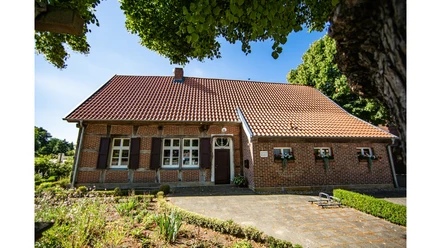 Töddenhaus Beesten MAE.jpg Backsteinhaus mit rotem Ziegeldach, weißen Fenstern und Blumenschmuck im grünen Umfeld.