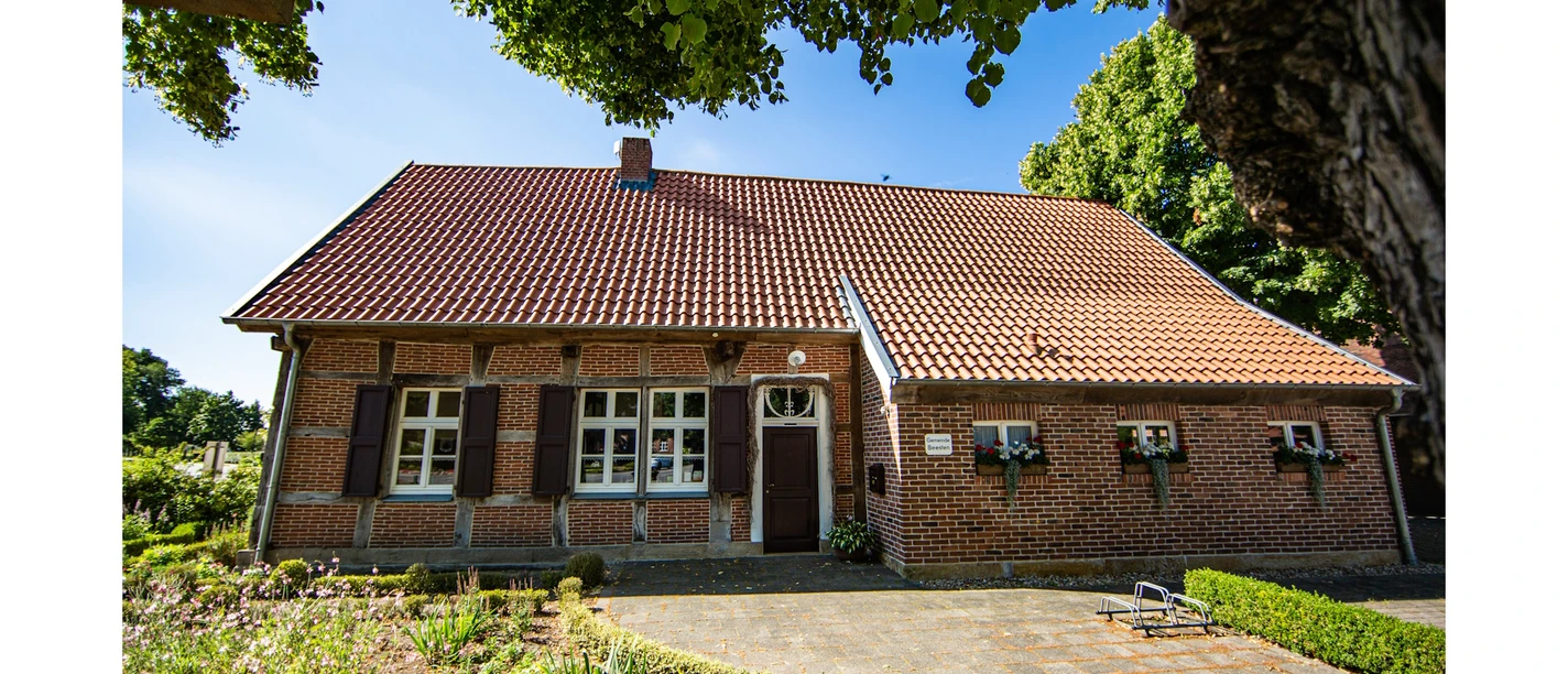 Töddenhaus Beesten MAE.jpg Backsteinhaus mit rotem Ziegeldach, weißen Fenstern und Blumenschmuck im grünen Umfeld.