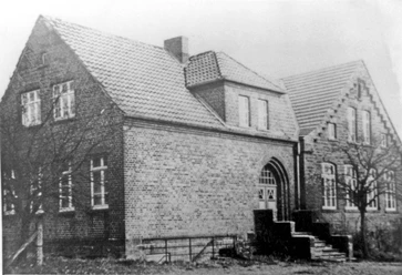 oberbauerschaft-dorfgemeinschaftshaus-alt.jpg Historisches Backsteingebäude mit Satteldach und Treppenstufen am Eingang, umgeben von kahlen Bäumen.