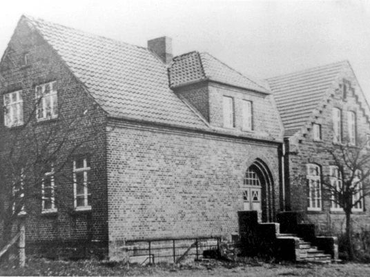 oberbauerschaft-dorfgemeinschaftshaus-alt.jpg Historisches Backsteingebäude mit Satteldach und Treppenstufen am Eingang, umgeben von kahlen Bäumen.