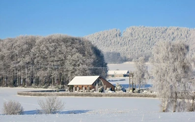 oberbauerschaft-friedhof-niedringhausen-01.jpg Schneebedeckter Friedhof mit Kapelle, umgeben von schneebehangenen Bäumen unter klarem Himmel.