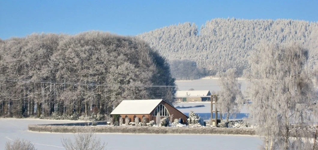 oberbauerschaft-friedhof-niedringhausen-01.jpg Schneebedeckter Friedhof mit Kapelle, umgeben von schneebehangenen Bäumen unter klarem Himmel.