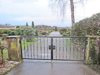 oberbauerschaft-friedhof-niedringhausen-03.jpg Schwarzes Eisentor durchtrennt gepflegten Weg auf einem Friedhof umrahmt von vielfältigem Grün.