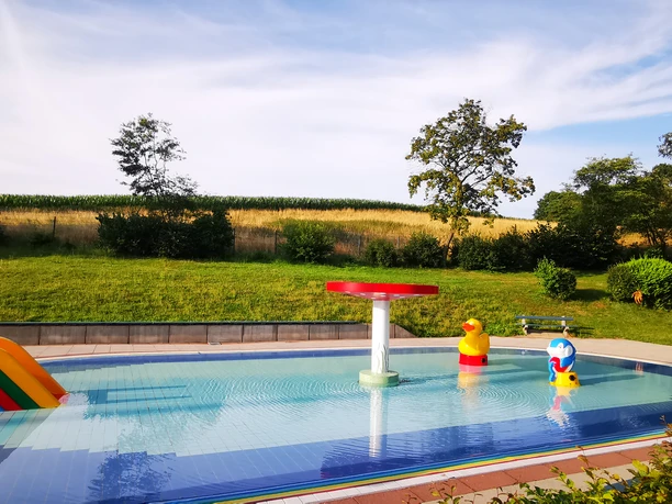 Kinderbecken mit flachem Wasser, bunten Wasserspielzeugen und umgeben von grünen Rasenflächen.