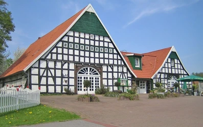 oberbauerschaft-niedermeiers-hof.jpg Zwei große Fachwerkgebäude mit roten Ziegeldächern und grünem Giebel bei klarem Himmel.