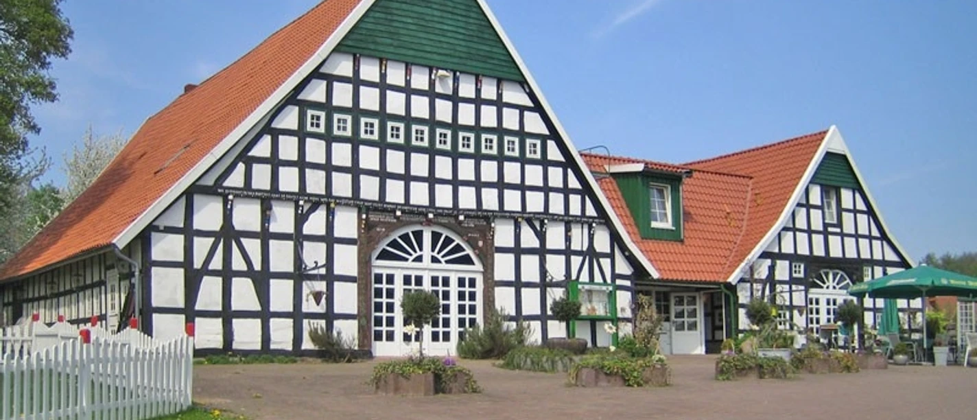 oberbauerschaft-niedermeiers-hof.jpg Zwei große Fachwerkgebäude mit roten Ziegeldächern und grünem Giebel bei klarem Himmel.