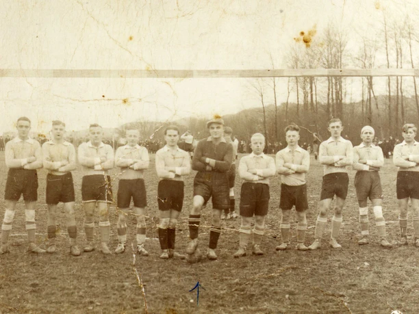 oberbauerschaft-alter-sportplatz-02.jpg Eine historische Fußballmannschaft posiert geschlossen in zwei Reihen vor einem Tor auf einem ländlichen Spielfeld.