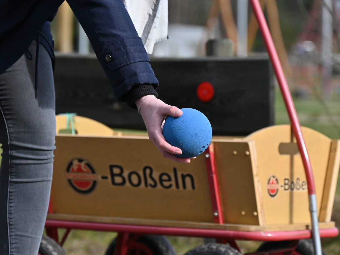 Boßeln in SHS_15_CC-BY-SA_Teutoburger_Wald_Stadt_Schloß_Holte-Stukenbrock.JPG Person hält blaue Boßelkugel vor einem Handwagen mit Boßeln-Schriftzug in Schloß Holte-Stukenbrock.