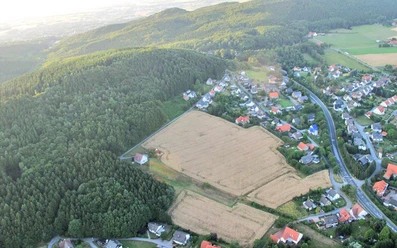 oberbauerschaft-koepperplatz-01.jpg Luftaufnahme eines Weilers mit Feldern und dichtem Wald, umgeben von sanft geschwungenen Hügeln.
