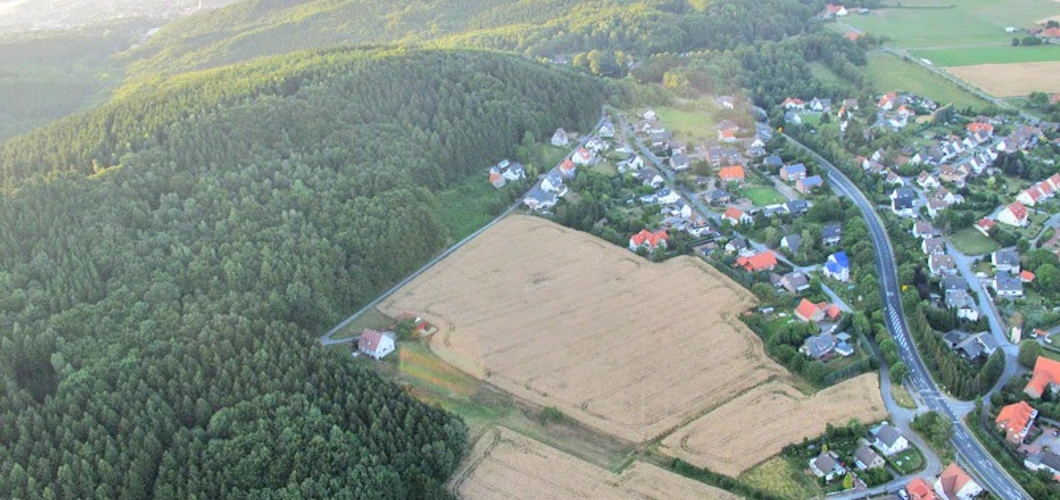 oberbauerschaft-koepperplatz-01.jpg Luftaufnahme eines Weilers mit Feldern und dichtem Wald, umgeben von sanft geschwungenen Hügeln.