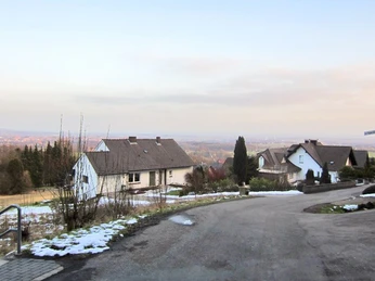oberbauerschaft-koepperplatz-02.jpg Verschneite Landschaft mit zwei Häusern, Bäumen und einem kurvigen Weg, im Hintergrund Weitsicht.