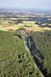 oberbauerschaft-wittekindsbruecke-01.jpg Luftaufnahme eines Dorfes, umgeben von dichten Wäldern und Feldern, mit Straßenverlauf im Vordergrund.
