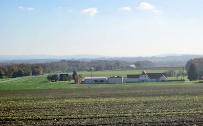 oberbauerschaft-blick-ins-ravensberer-land-01.jpg Weiter Blick über ein landwirtschaftliches Areal mit Feldern, vereinzelten Gebäuden und bewaldeten Hügeln.