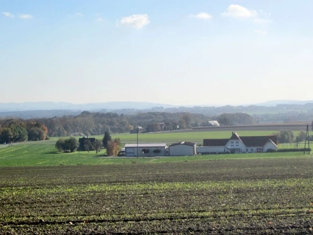 oberbauerschaft-blick-ins-ravensberer-land-01.jpg Weiter Blick über ein landwirtschaftliches Areal mit Feldern, vereinzelten Gebäuden und bewaldeten Hügeln.