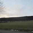 oberbauerschaft-hilgenstuhl.JPG Weites Feld vor einer sanft ansteigenden Waldlandschaft unter bewölktem Himmel in Oberbauerschaft.